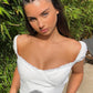 Woman wearing a white off-shoulder top with green foliage in the background