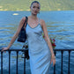 Woman in a light blue dress standing by a lake with a mountain in the background.