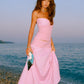 Woman in a pink dress standing on a pebbly beach with ocean and sky in the background