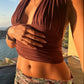 Woman in a brown halter top and patterned skirt standing by a pool with a scenic view.