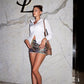Woman in a stylish outfit standing in front of a YSL logo on a marble wall.