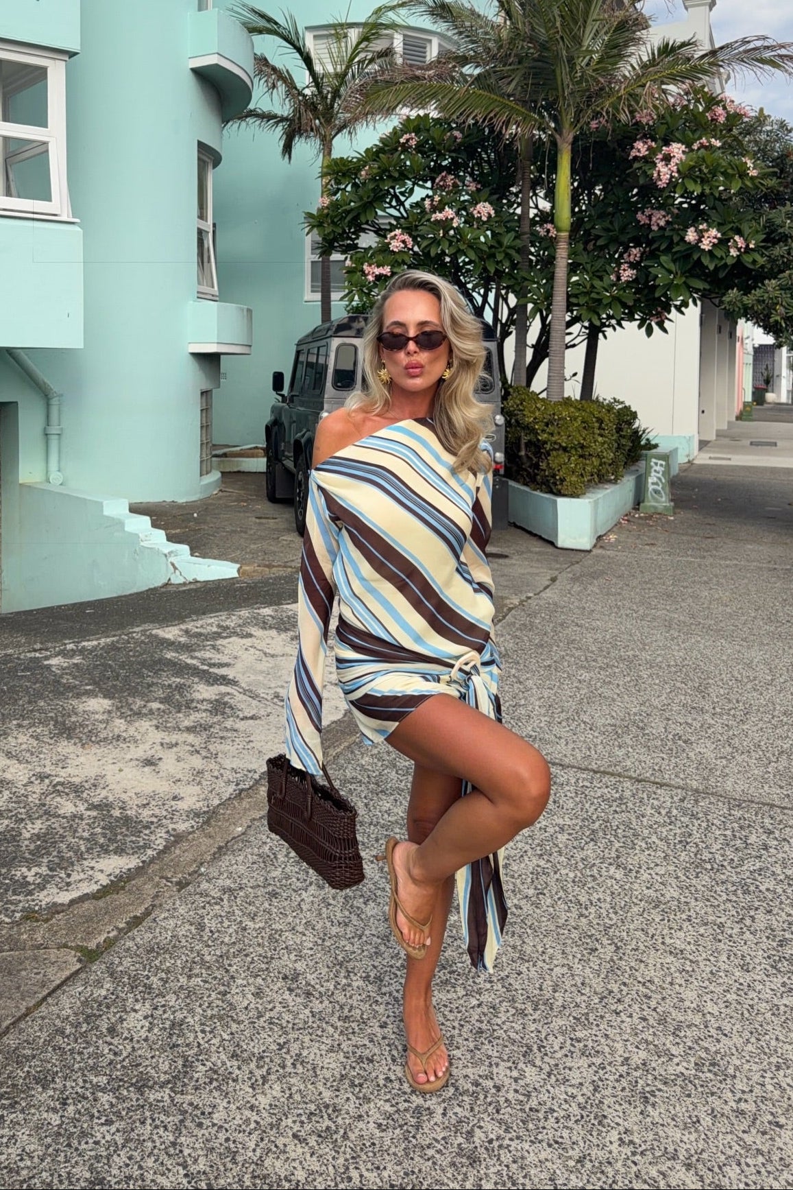 Woman in a striped dress posing on a street with a teal building and palm trees in the background