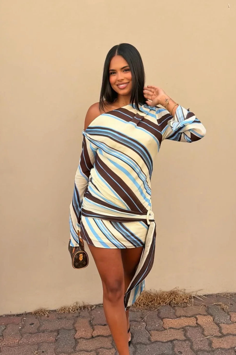 Woman wearing a striped dress posing against a beige wall.